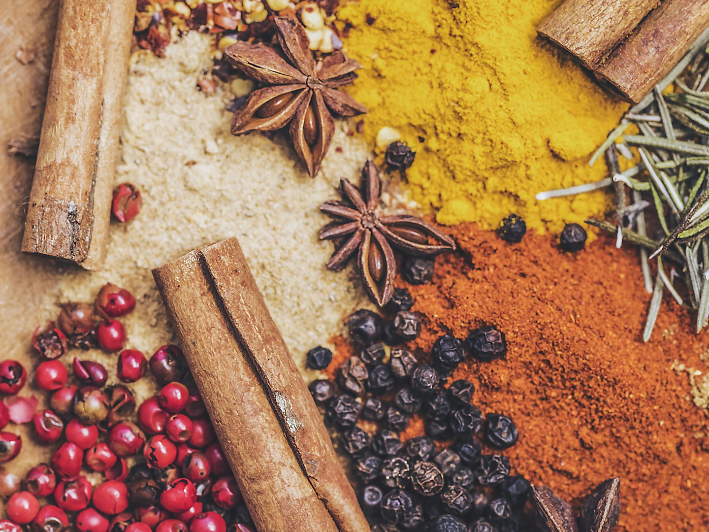 Cinnamon sticks, star anise, peppercorns and ground spices spread on a table.