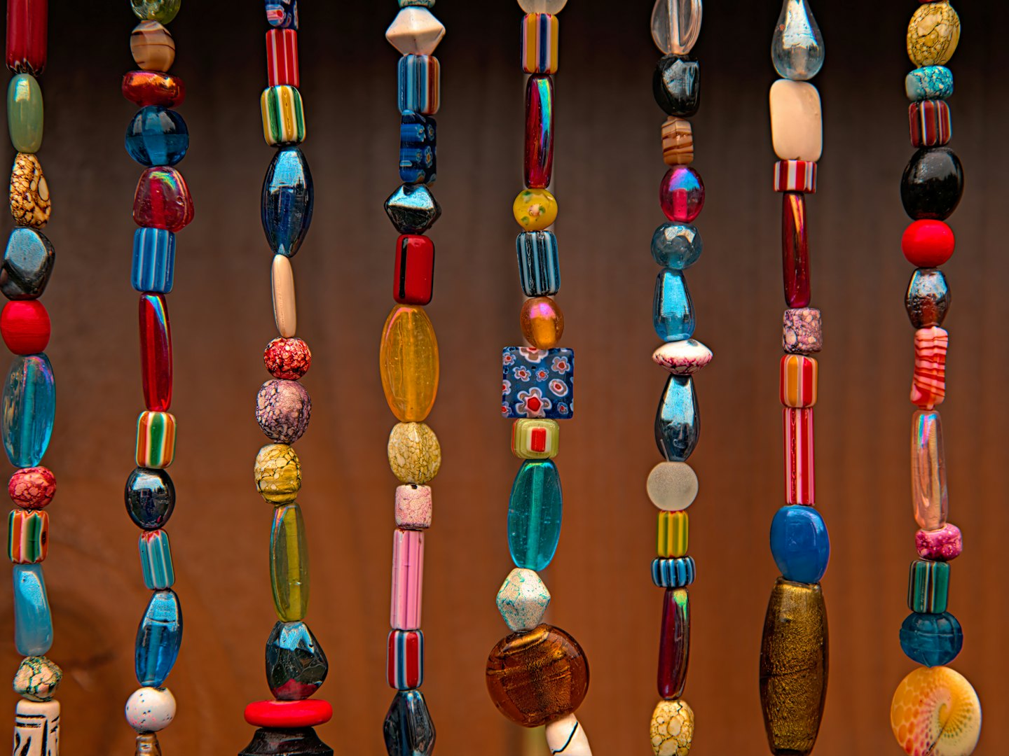Strings of coloured glass beads hanging against a wooden wall.