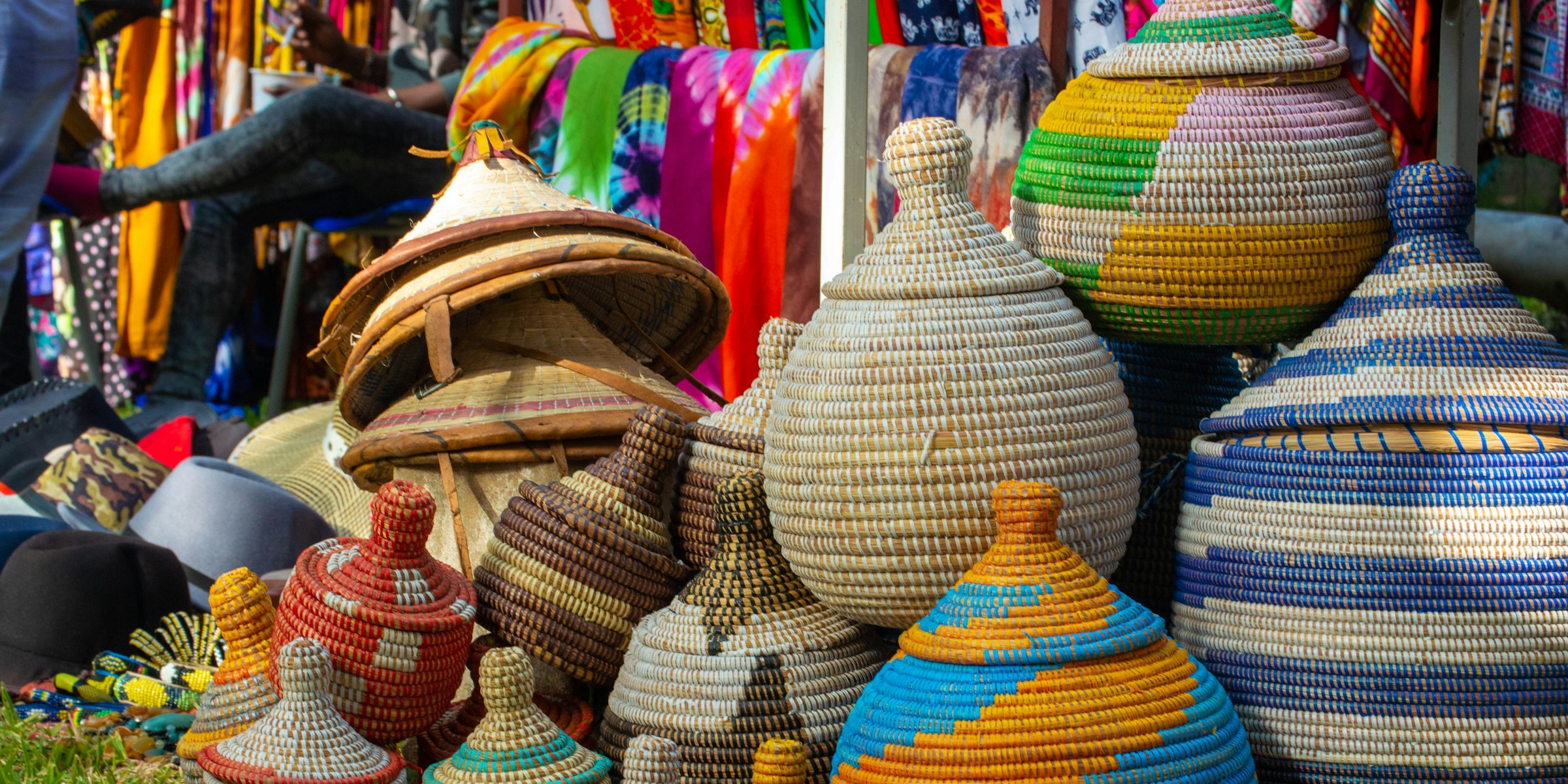Colourful woven baskets with pointed lids stacked on the grass at a craft stall.